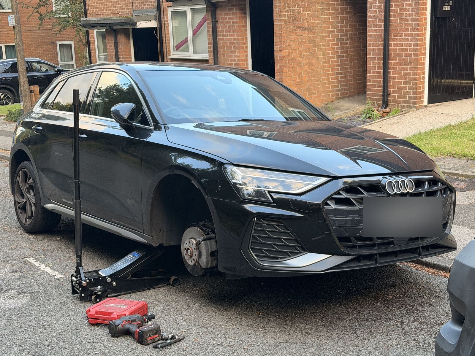 Car with its front wheel removed on a residential street, with jack and impact wrench