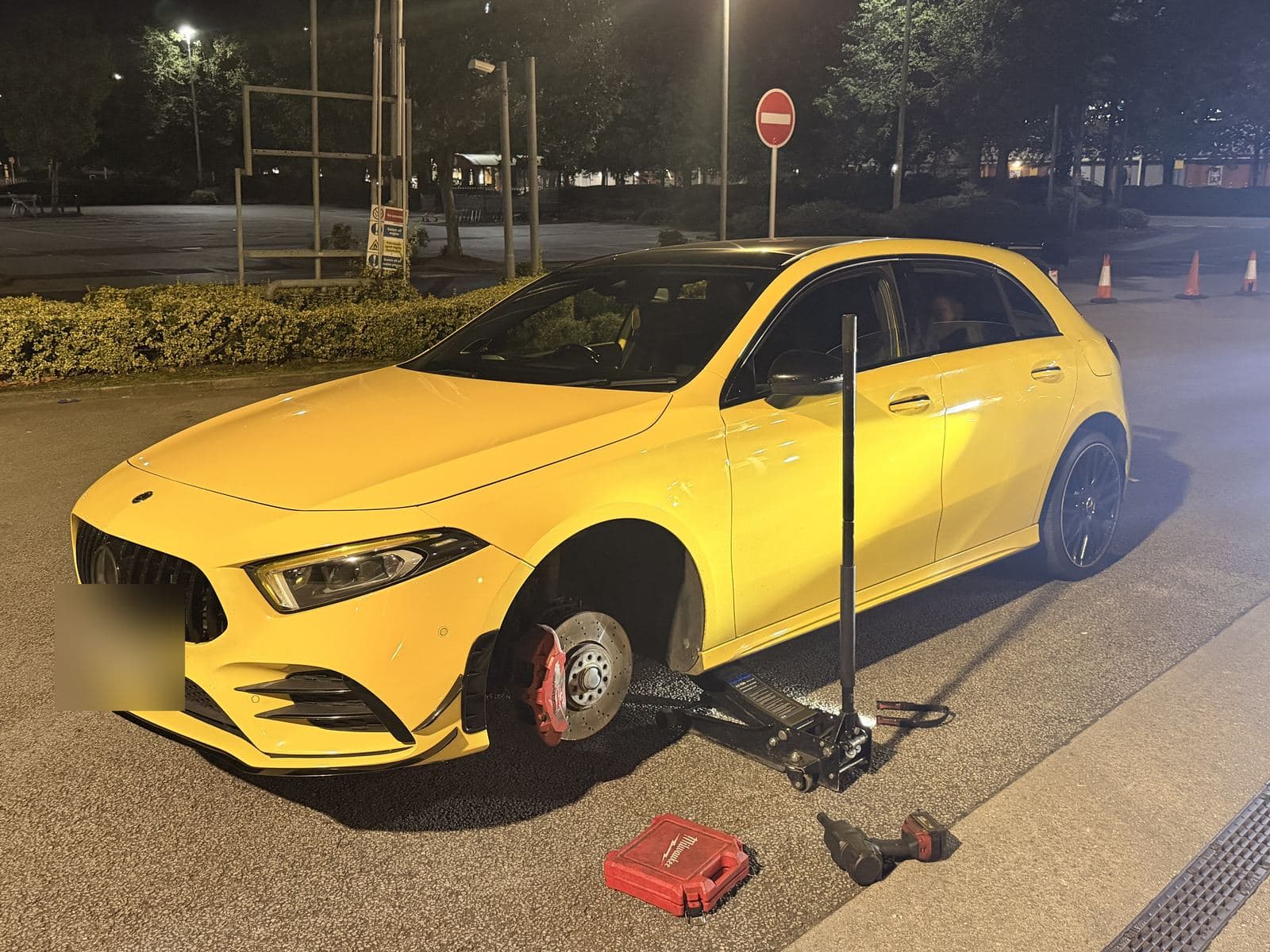 Car with its front wheel removed in a car park at night