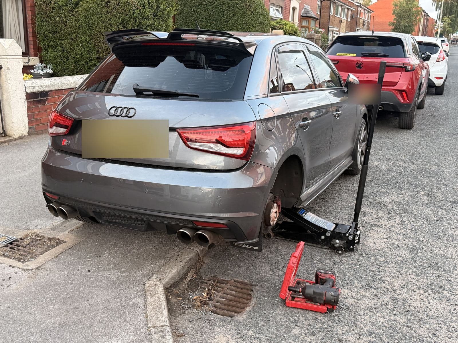 Hatchback with its rear wheel removed while parked on a street